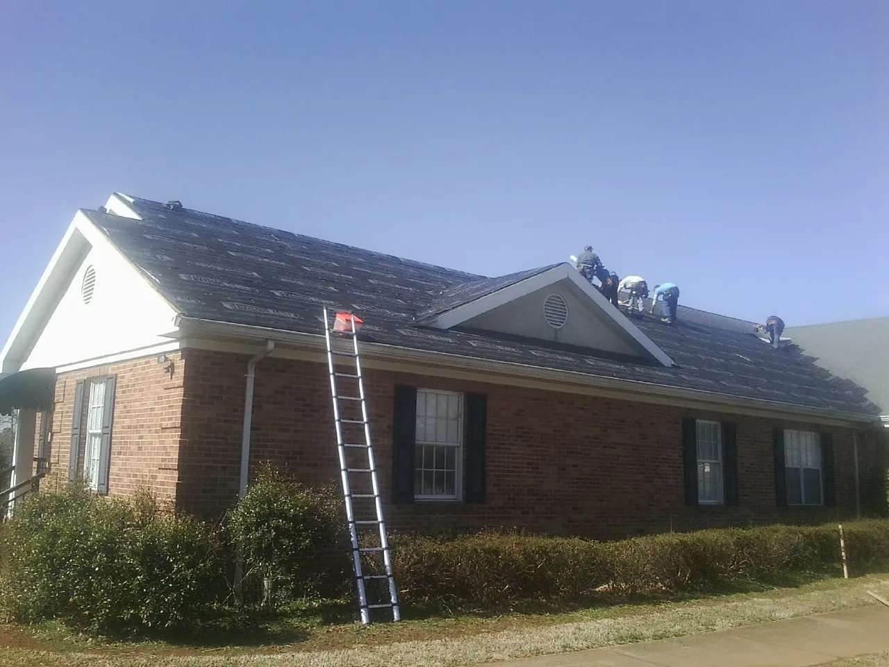 Crew tearing shingles off a brick ranch roof with a ladder set — Emergency Roof Repair work by our crew in Conowingo