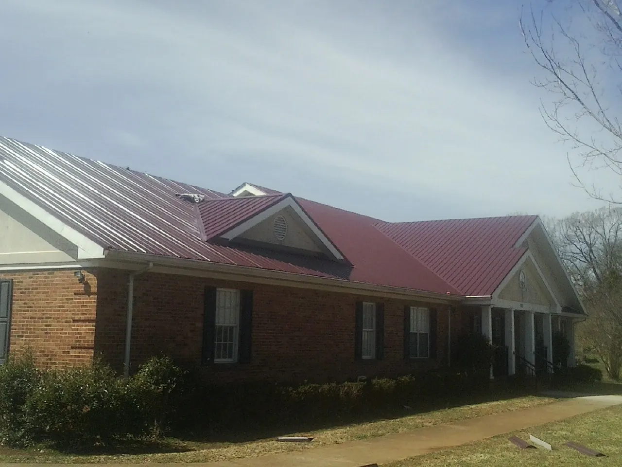 Red metal roof with gabled entries on a long brick building, from a Hail Damage Roof Repair job in Conowingo