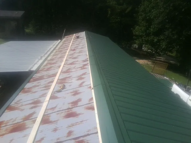 Old rusted panels beside newly installed green metal roofing — Wind Damage Roof Repair by Roofing Brothers in Conowingo