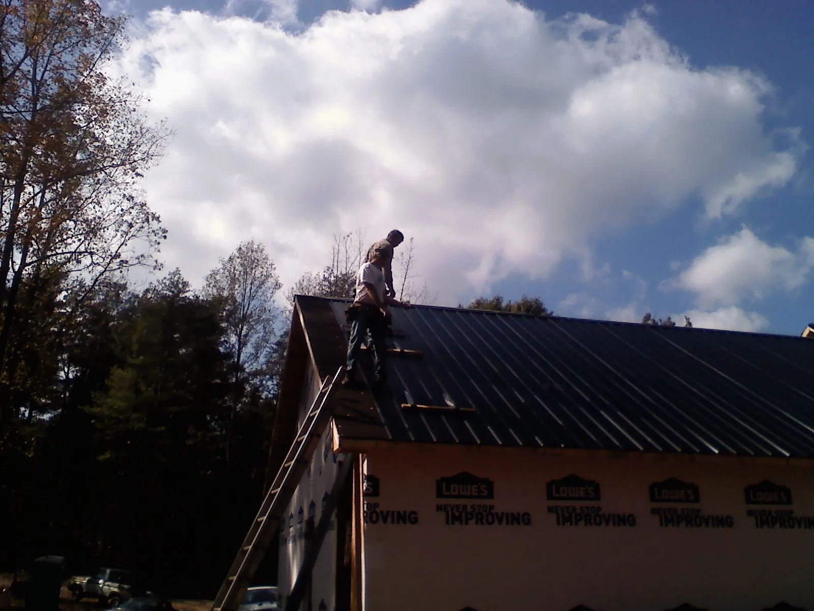 Roofer fastening dark metal panels high against a cloudy sky, from a Roof Inspection job in Conowingo